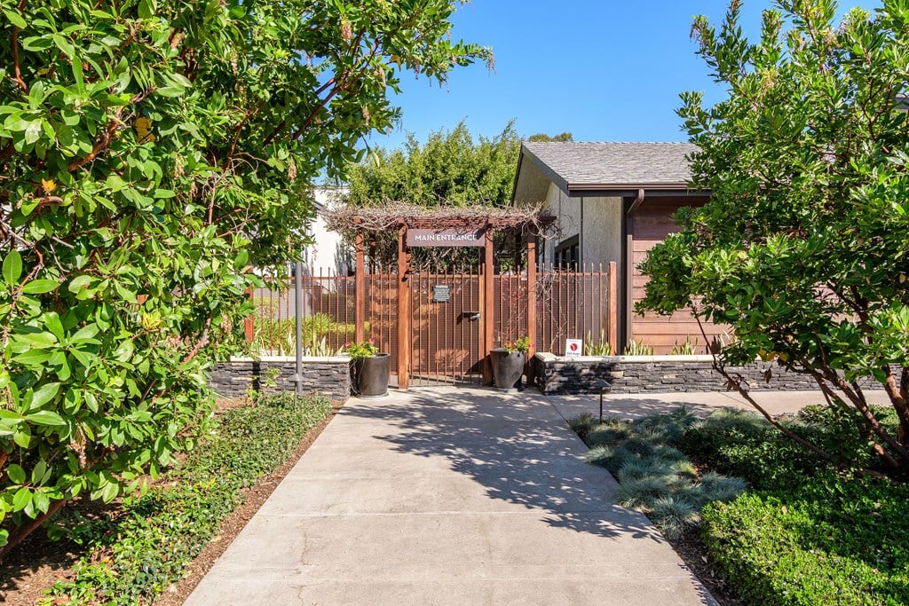A small building with a brown fence and gate is surrounded by green bushes.