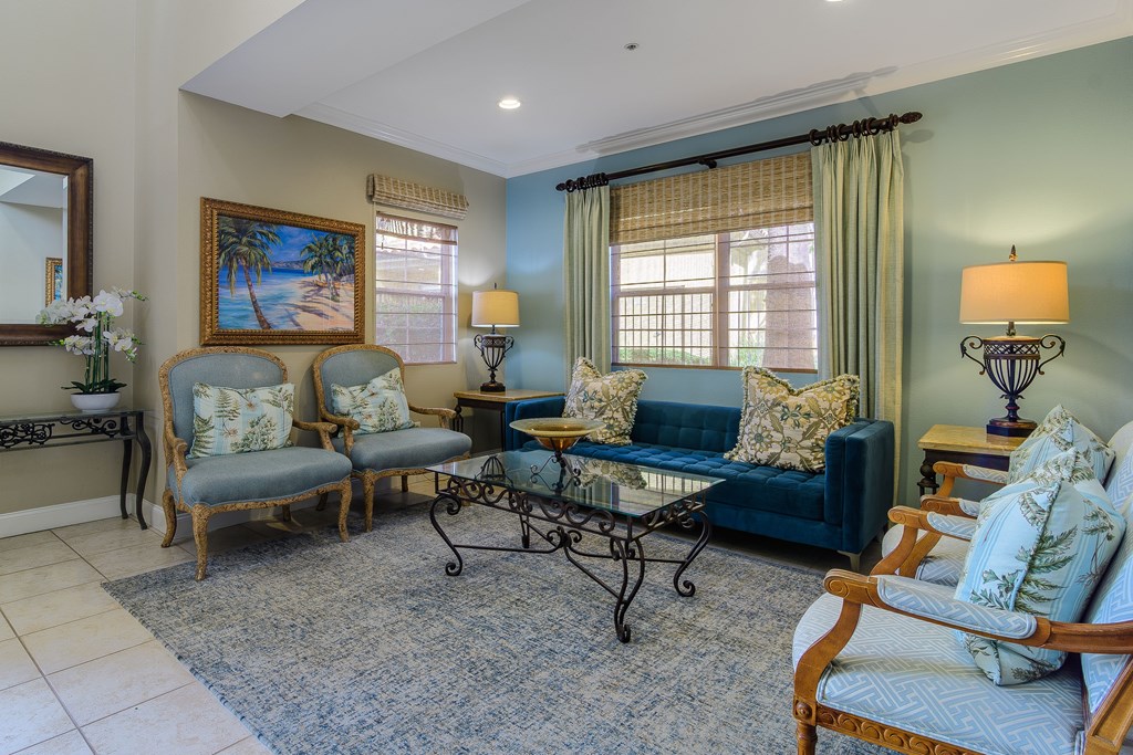 A living room with a blue couch and a painting of a beach scene on the wall.