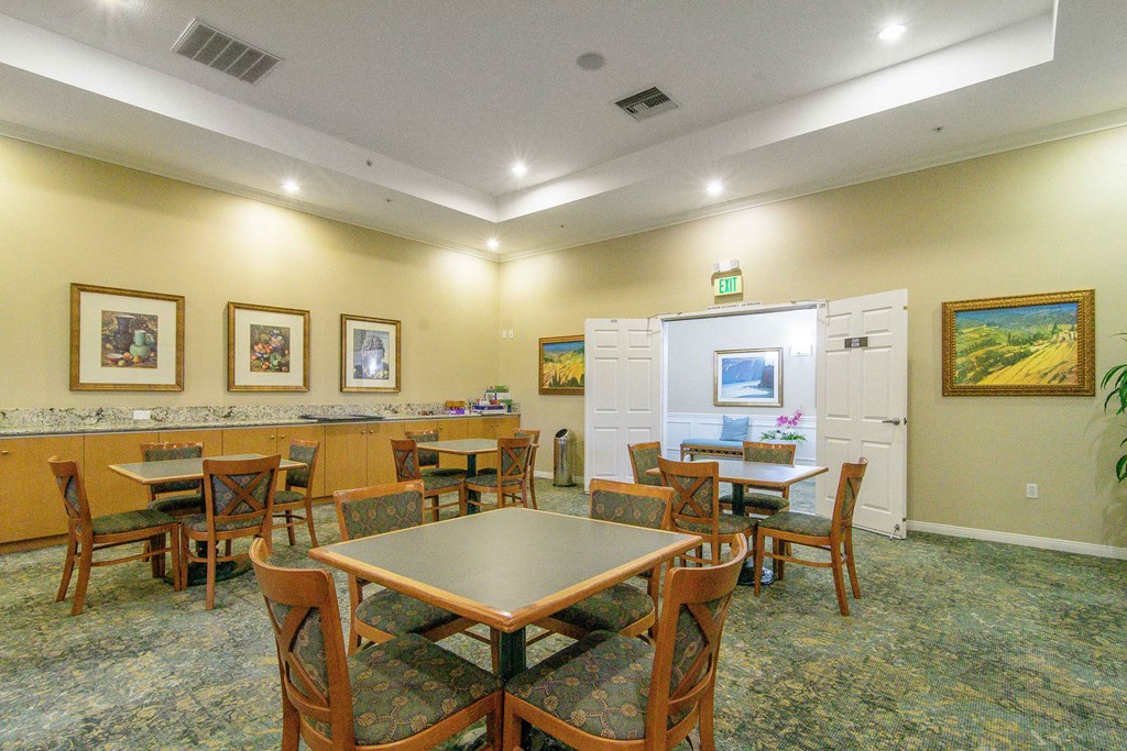 A room with a table and chairs in the foreground and a framed painting on the wall.