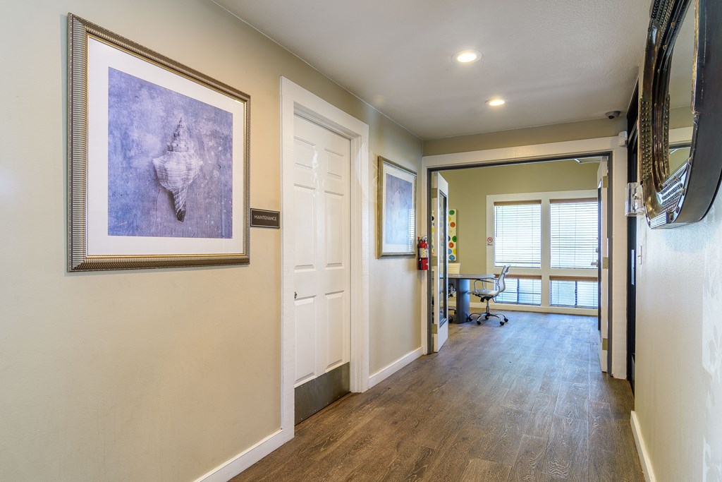 A hallway with a painting on the wall and a mirror on the right side.