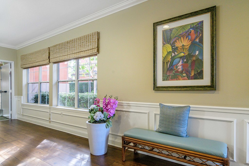 A room with a bench, a vase with flowers and a picture on the wall.