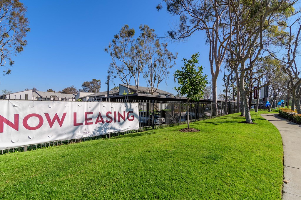 A leasing sign is displayed on a fence in front of a building.