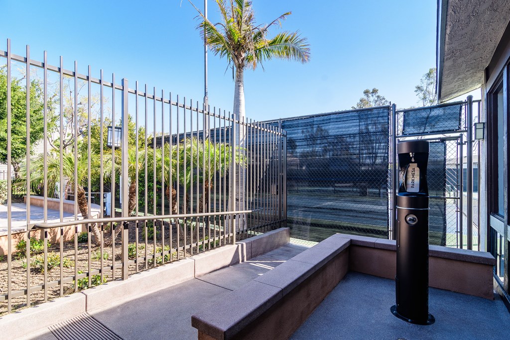 A metal fence with a bench and a trash can in front of a building.