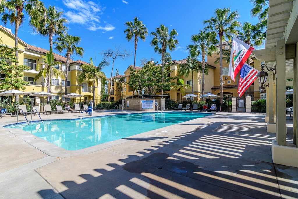A pool surrounded by palm trees and a building with an American flag.