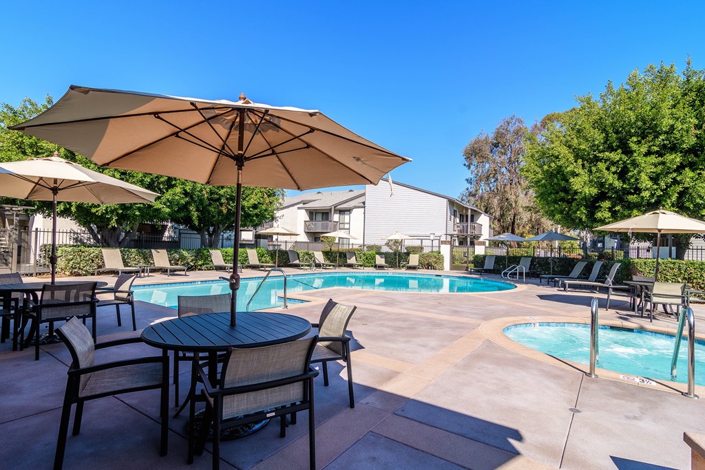 A pool area with a table and chairs and umbrellas.