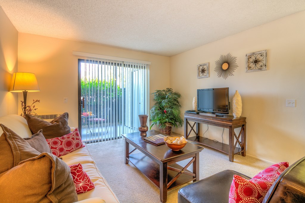 A living room with a couch, a coffee table, a television, and a window with blinds.