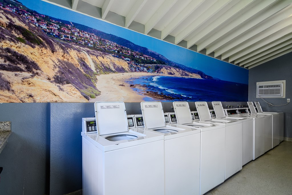 A row of washing machines in front of a wall mural.