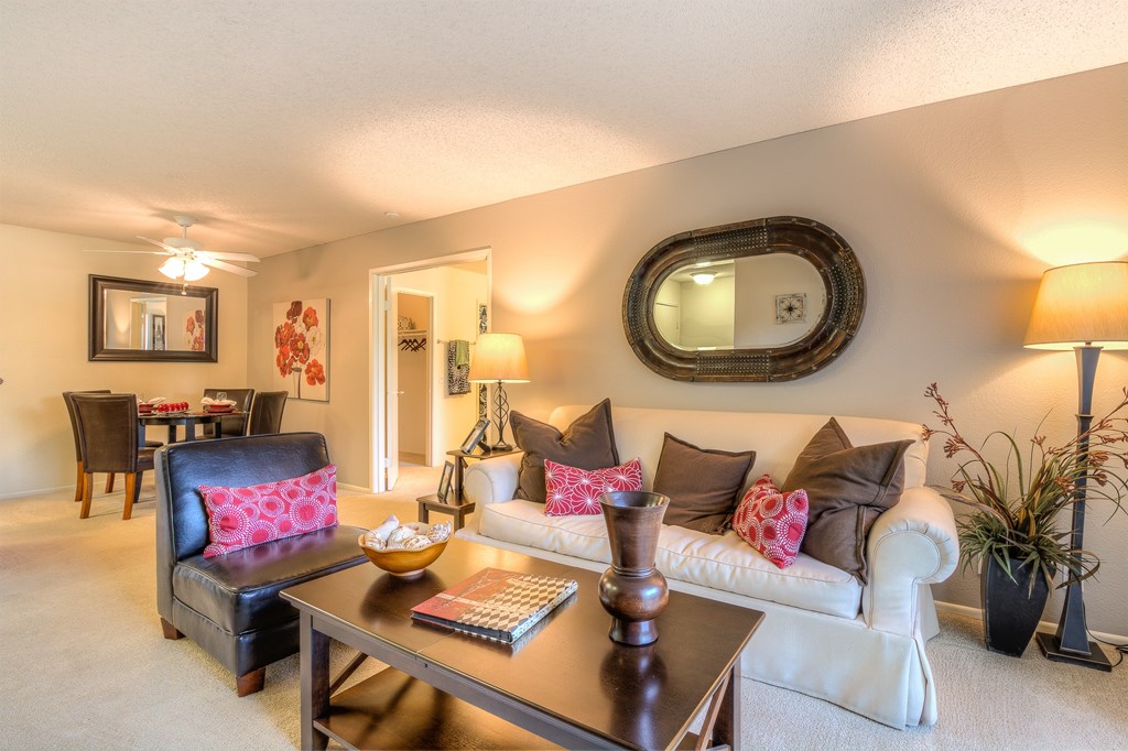 A living room with a black leather chair and a white couch with pink pillows.