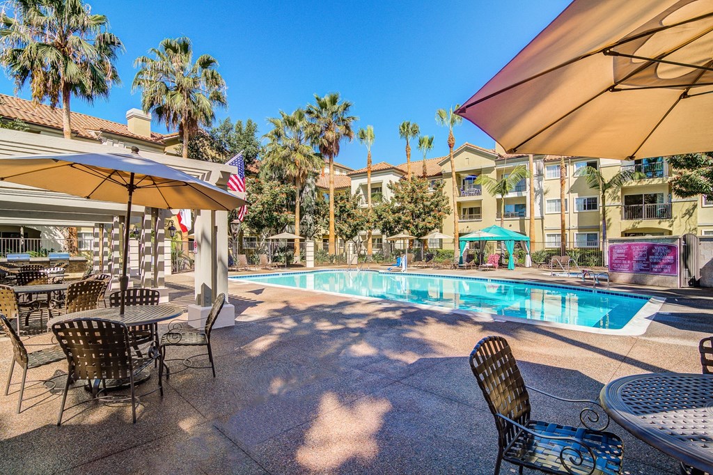 a swimming pool with tables and umbrellas and buildings in the background
