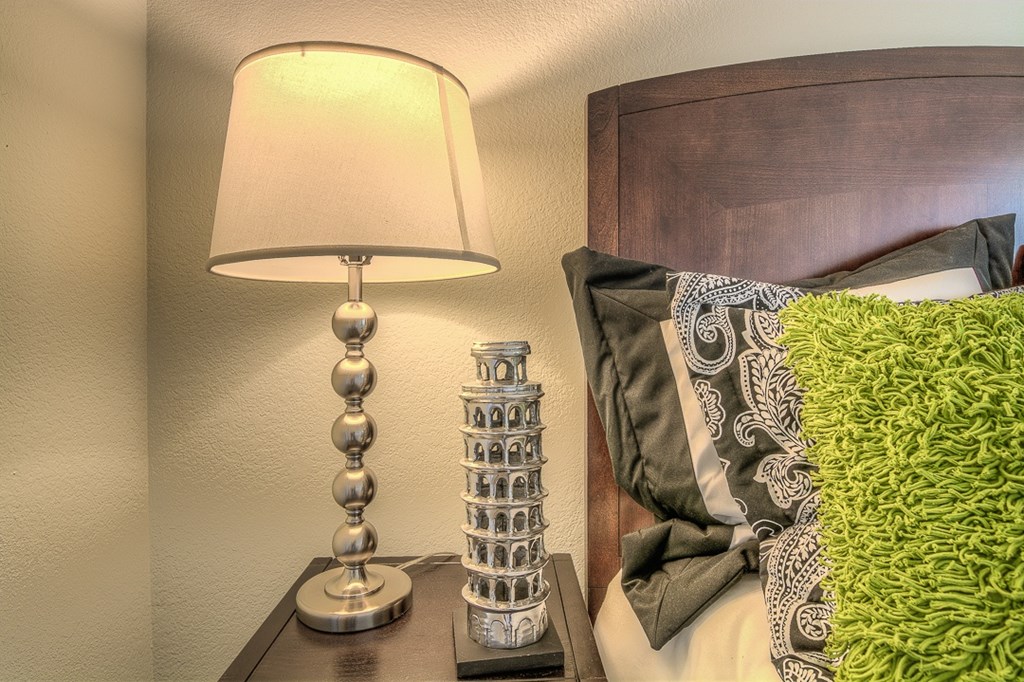 A lamp with a base of silver balls is on a bedside table next to a green pillow.