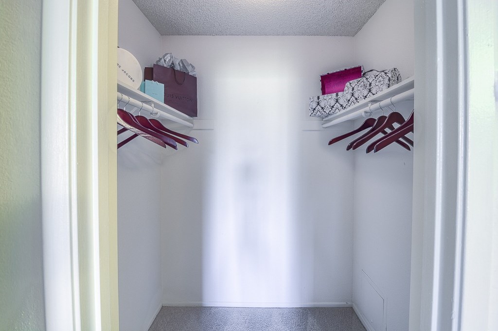 A white closet with clothes hanging on the shelves.