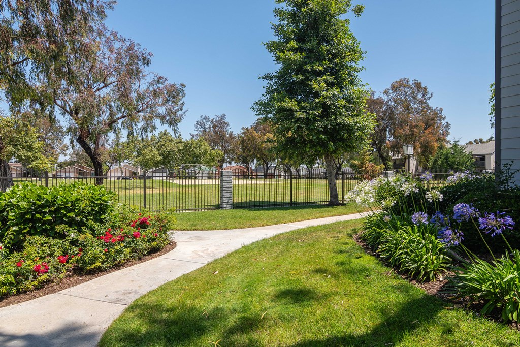 a walkway through a park with flowers and a fence
