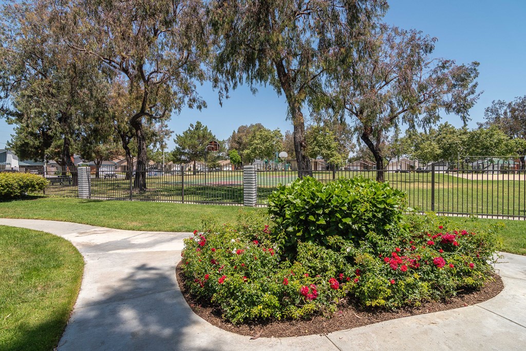 a park with a sidewalk and flowers and a fence