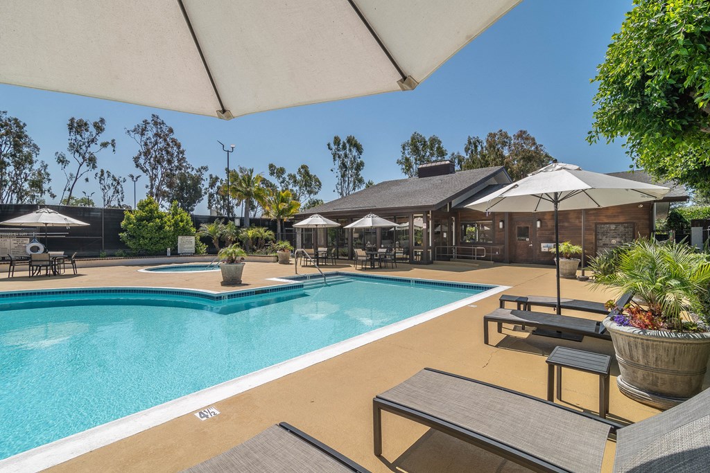 a swimming pool with tables and umbrellas and a building in the background