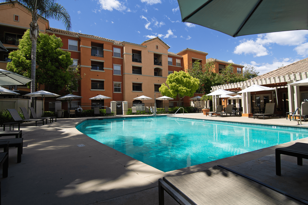 A large swimming pool surrounded by a patio with chairs and umbrellas.