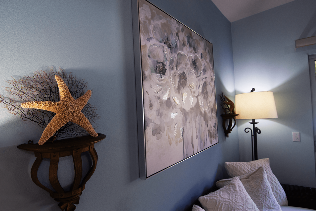 A starfish sits on a table next to a painting and a lamp.