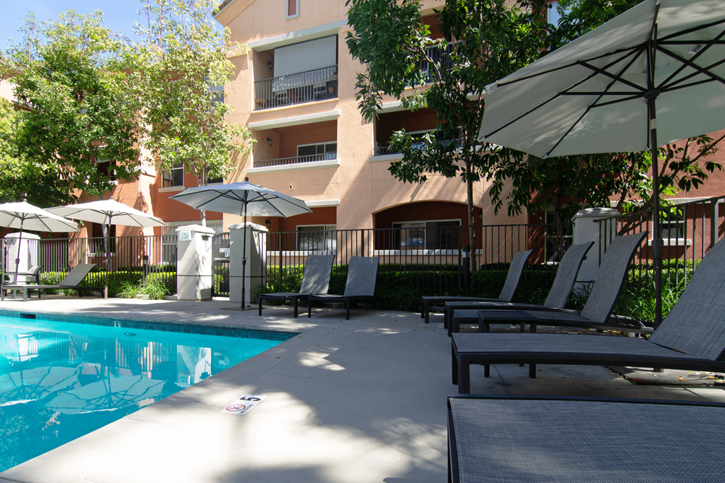 A pool surrounded by chairs and umbrellas with a building in the background.