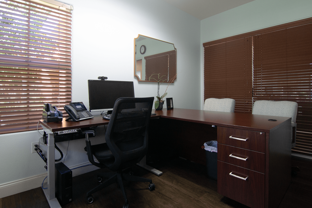 A black office chair is in front of a desk with a computer monitor, keyboard, and mouse.