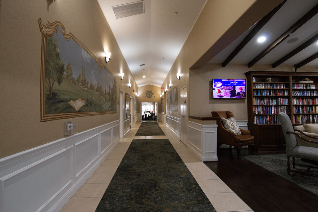 A long hallway with a painting on the wall and a TV on the wall.