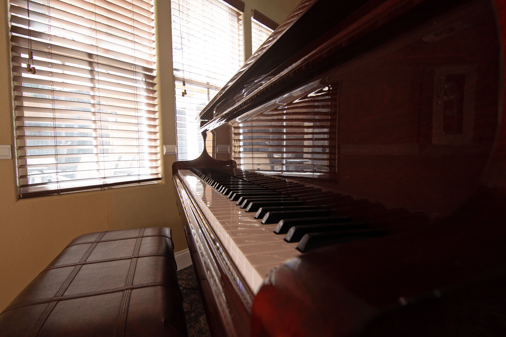 A brown piano sits in front of a window with blinds.