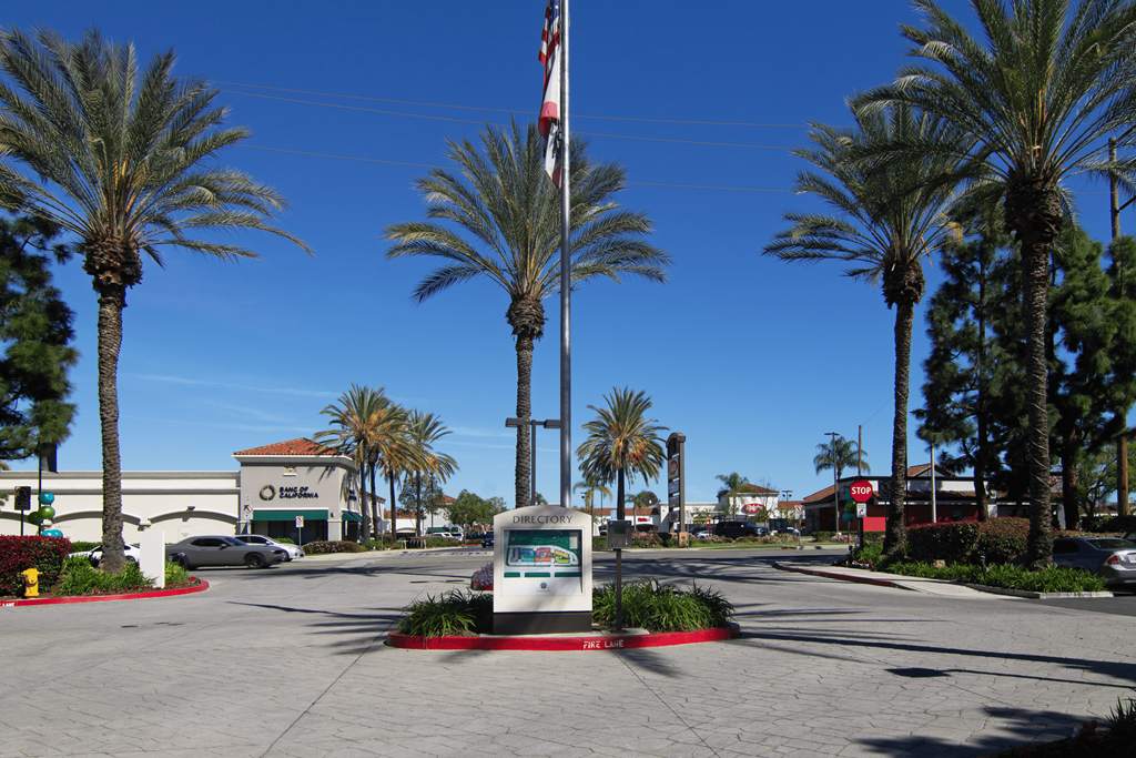 A sign in front of palm trees with a flag in the background.