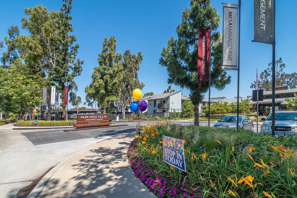 a park with flowers and trees and a sign with balloons on it