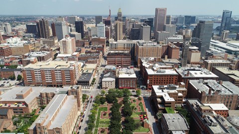 A cityscape with a mix of modern and older buildings, a green park area, and a clear sky.