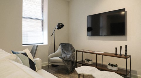 A modern living room with a white couch, a black TV, and a wooden shelf with plants.