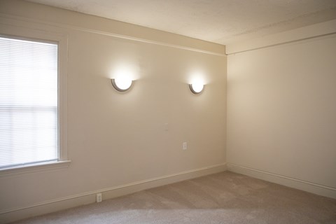A room with two lights on the wall and a window with blinds.