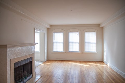 A large empty room with a fireplace and wooden floors.