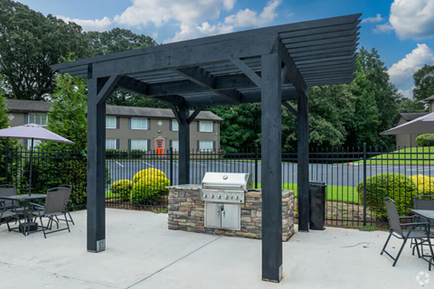 A patio with a grill and chairs under a black pergola.