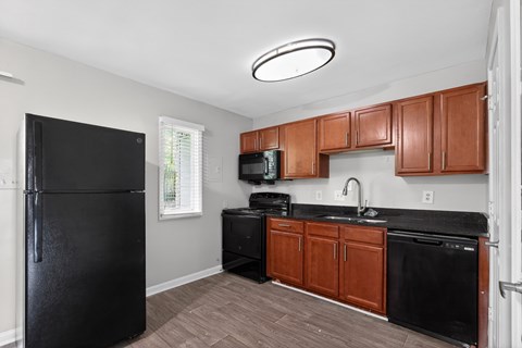 A black refrigerator stands in a kitchen with wooden cabinets and black countertops.