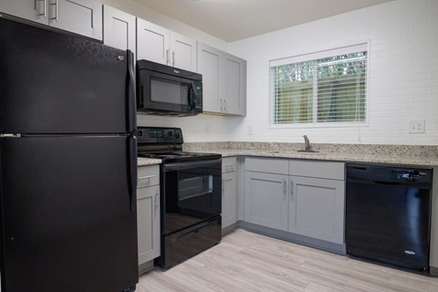 A black refrigerator stands in a kitchen with a black oven and microwave.