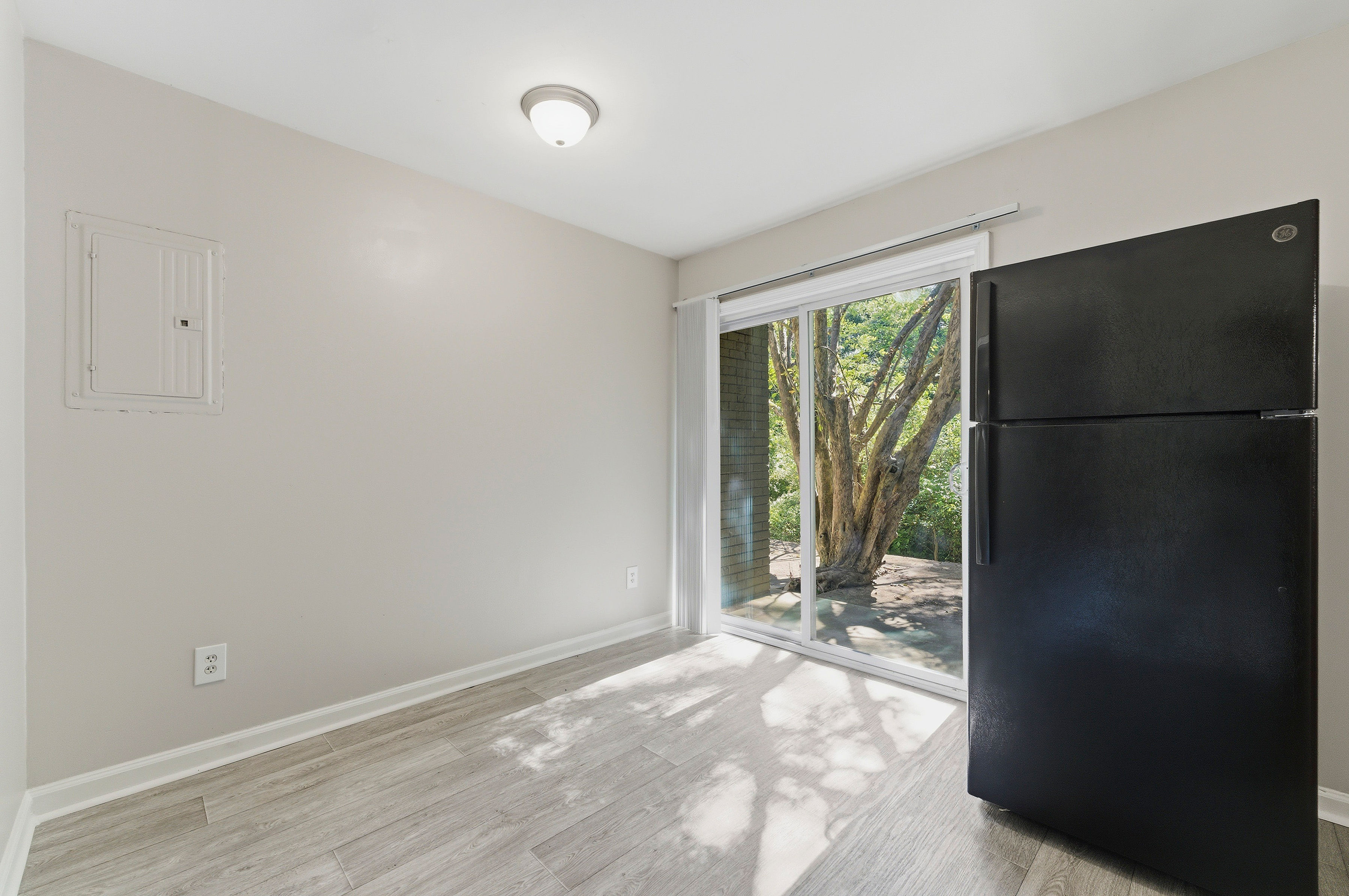 A black refrigerator is in a kitchen with a window that looks out to a tree.