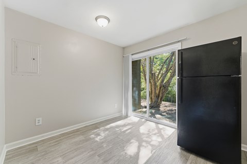 A black refrigerator is in a kitchen with a window that looks out to a tree.