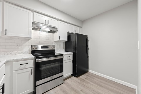 A black refrigerator stands in a kitchen with white cabinets and a black stove.