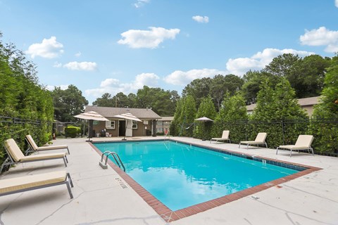 A pool surrounded by trees and lounge chairs.