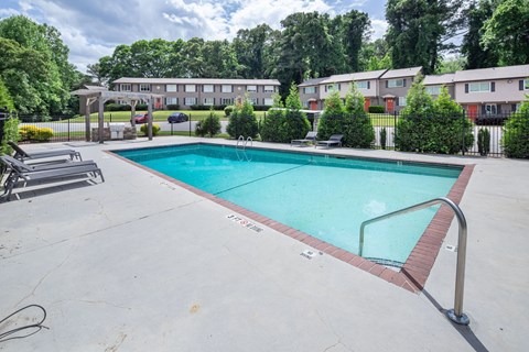 A swimming pool surrounded by a concrete patio and residential buildings.