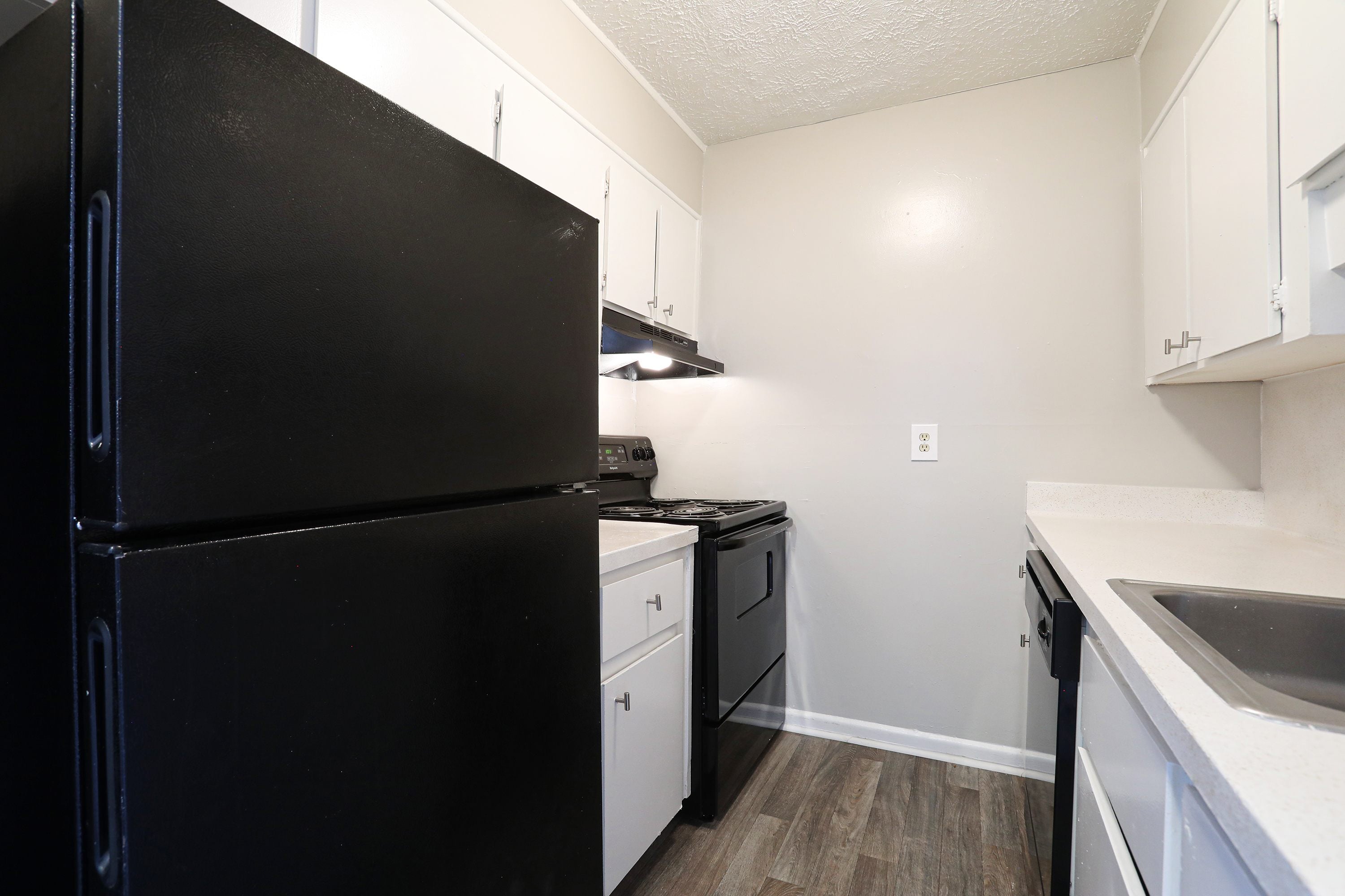 A black refrigerator is in a kitchen with white cabinets.