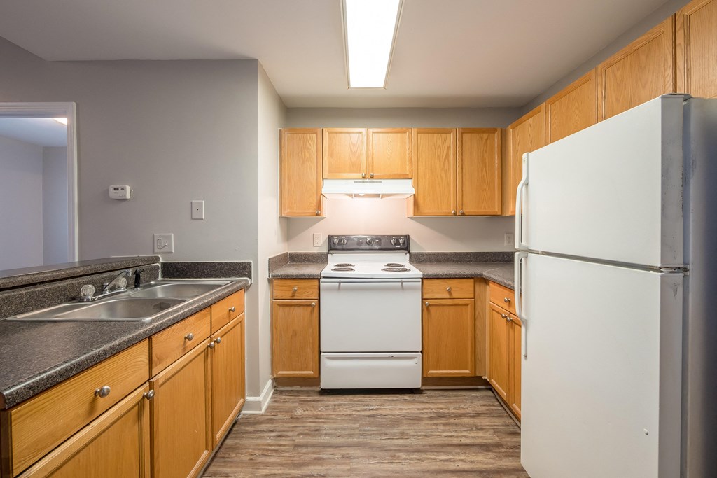 an empty kitchen with wood cabinets and white appliances at Crogman School Lofts, Atlanta
