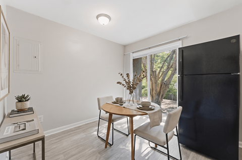A dining room with a table set for two and a view of trees outside the window.