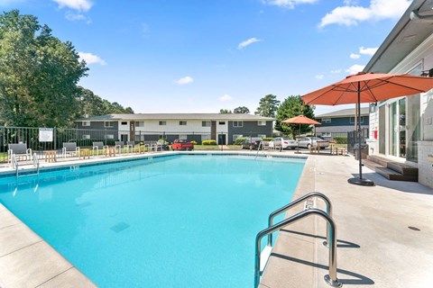 A large swimming pool with a metal ladder and a red umbrella.