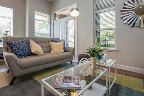 A grey couch with blue and yellow pillows sits in a living room with a glass coffee table in front of it.