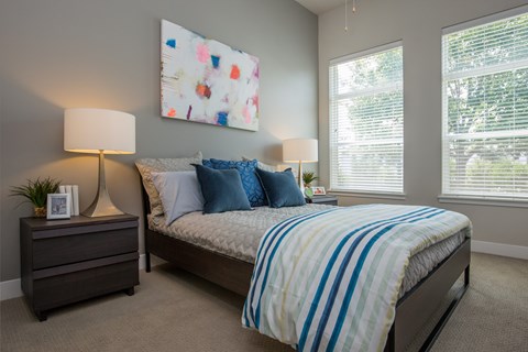 A bedroom with a bed, two lamps, and a painting on the wall.