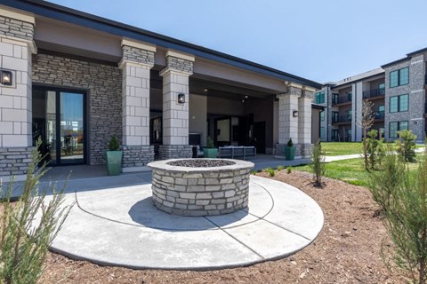 A modern building with a stone pillar and a circular fire pit in front.