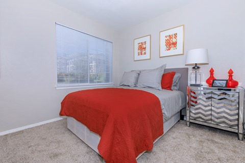 A bedroom with a bed covered in a red blanket and a grey blanket on top.