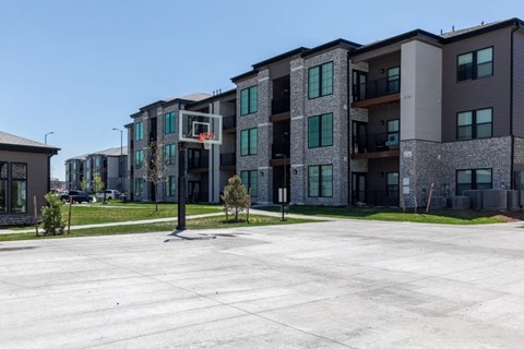 A basketball court is in the middle of a parking lot in front of apartment buildings.