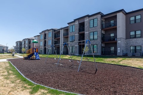 A playground with a swing set in front of apartment buildings.