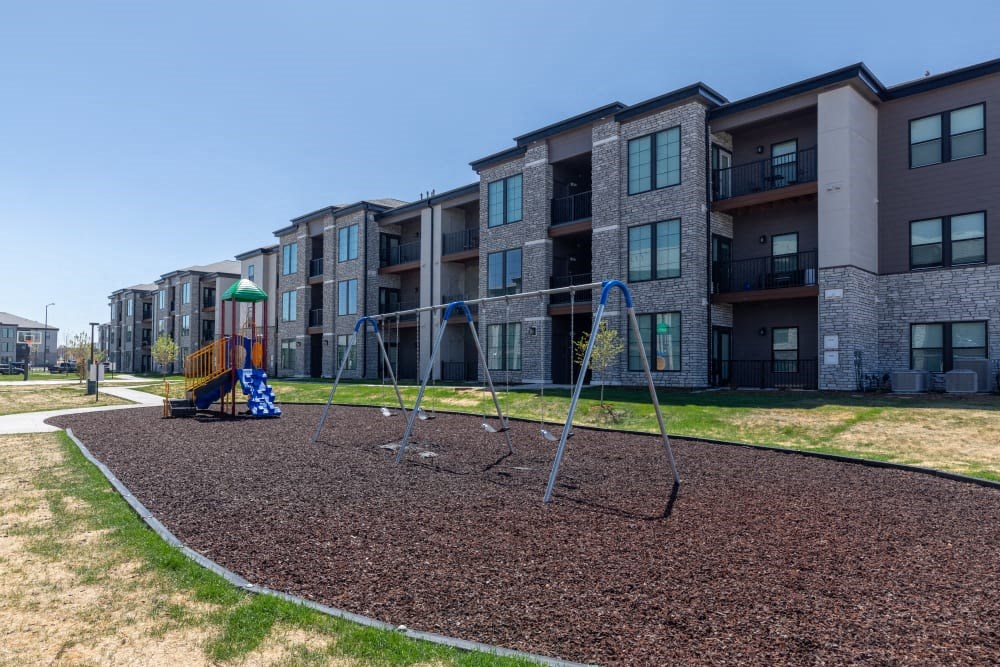 A playground with a swing set in front of apartment buildings.