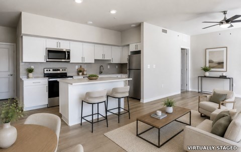A modern kitchen with white cabinets and appliances, a dining table with chairs, and a living area with a couch and coffee table.
